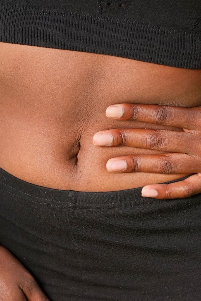 Close-up of a person holding their abdomen, indicating stomach discomfort, outdoors.